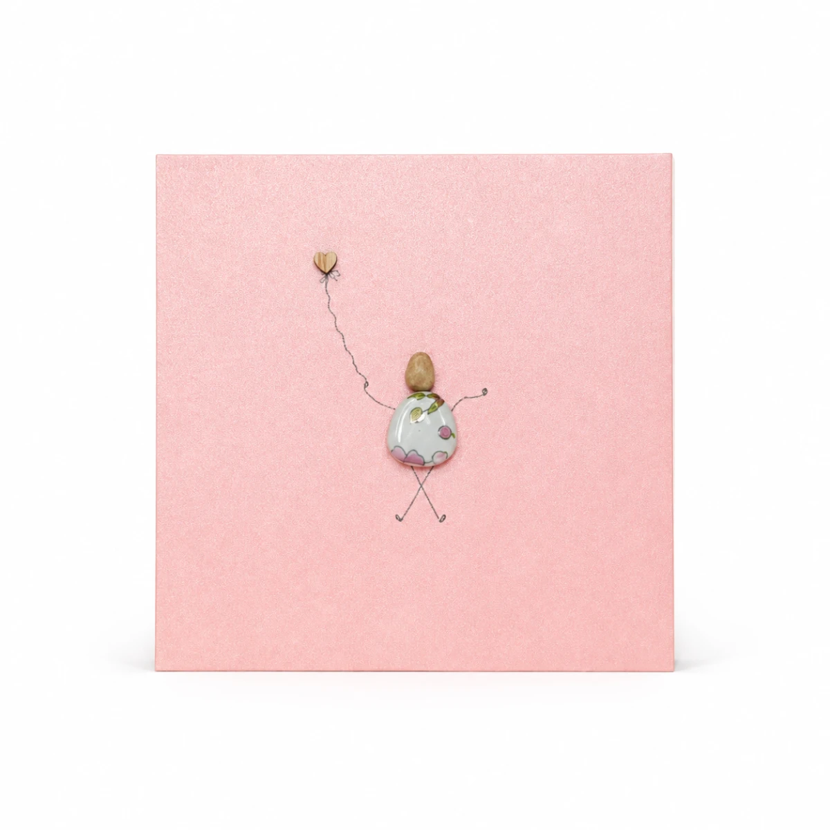 Pink handmade greeting card featuring a pebble figure holding a heart balloon