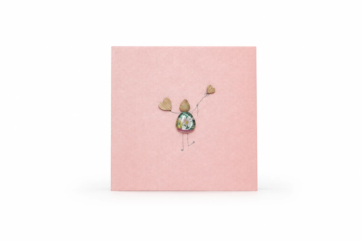 Pink handmade greeting card featuring a pebble figure holding two wooden hearts